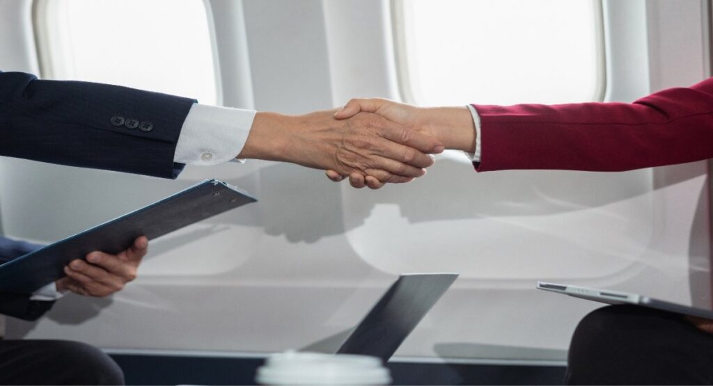Two business professionals in suits shaking hands inside a private jet