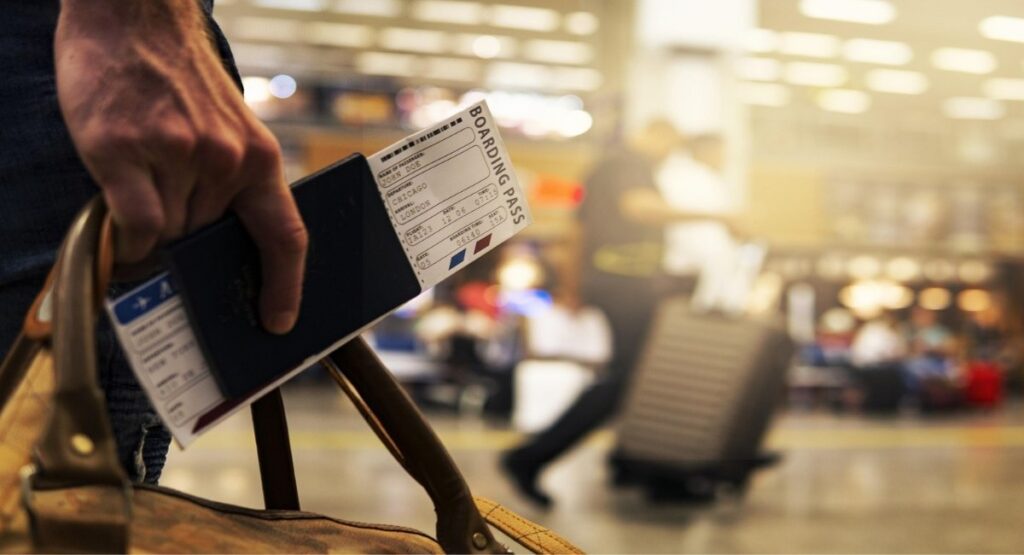 A business traveler holding a passport and a boarding pass at a busy airport terminal