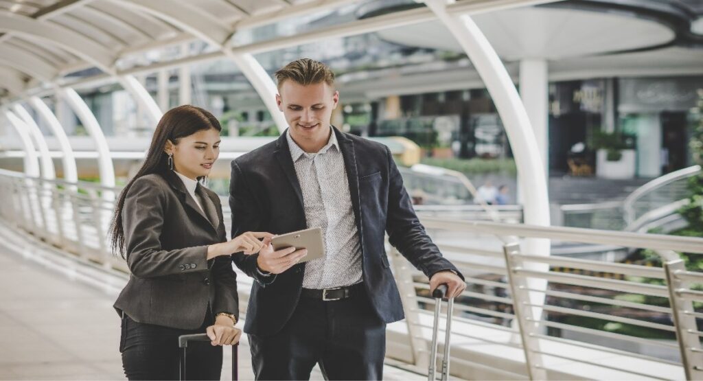 Two business travelers reviewing a corporate travel itinerary on a tablet at an airport