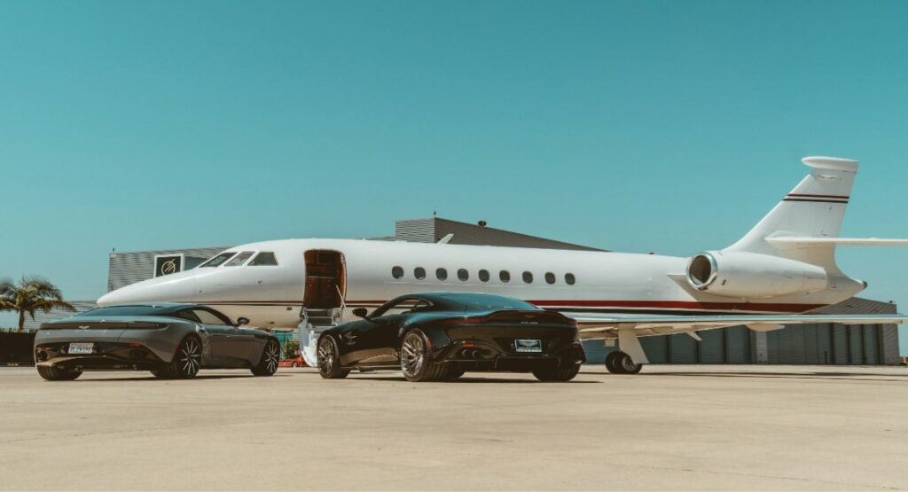 A private jet with luxury cars parked on a tarmac