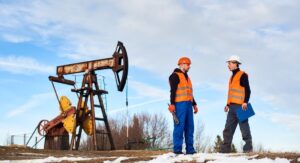 Oil field crew operators talking at an oil field with machinery in the background